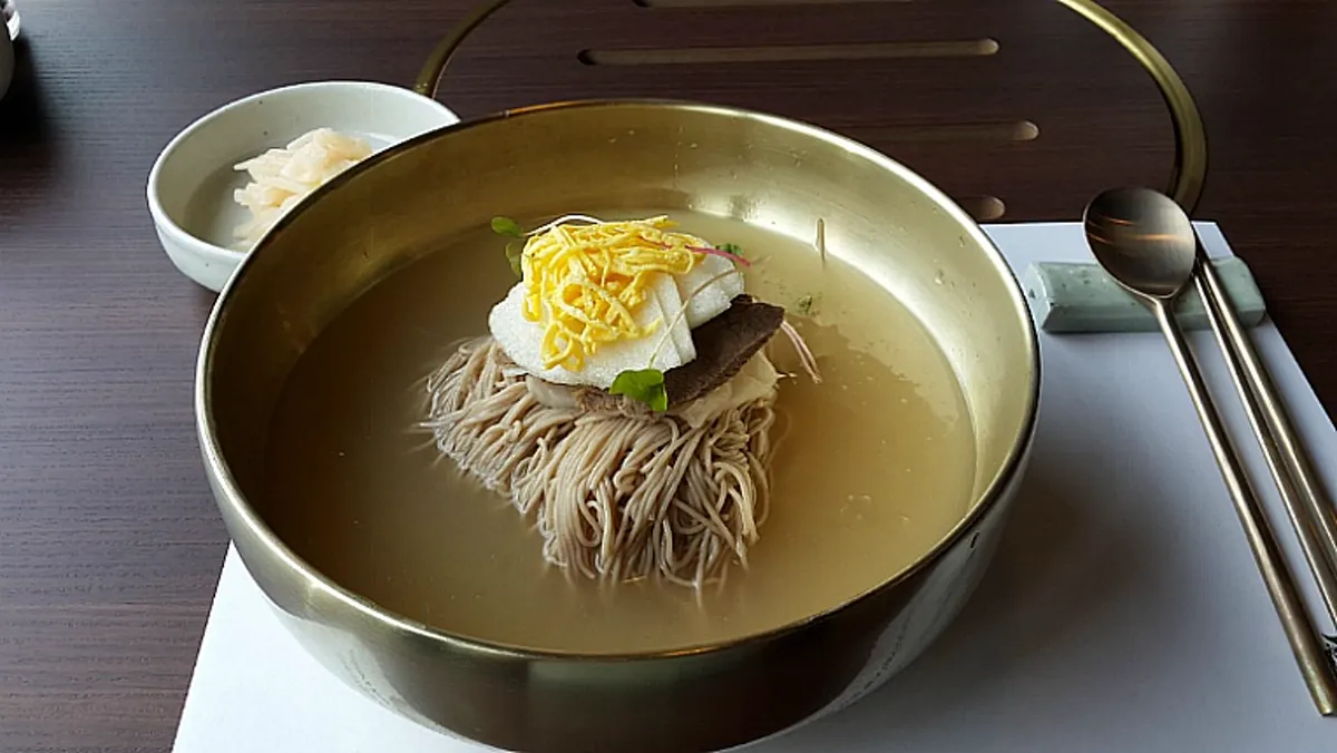 A bowl of Korean cold noodles (naengmyeon) in icy broth with egg and garnish