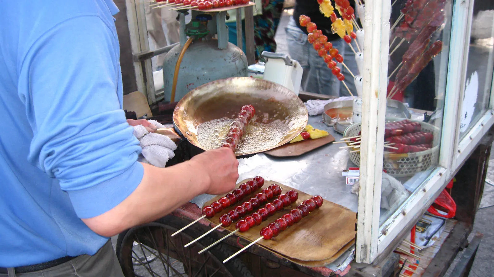 Street vendor dipping candied hawthorn (tanghulu) skewers into hot syrup, Tianjin, northern China